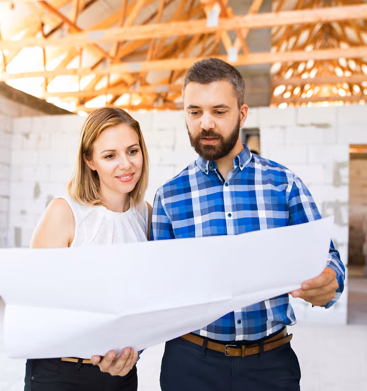 Un homme et une femme regardant attentivement un grand plan dans une maison en construction.