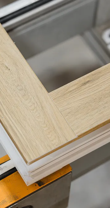 Gros plan de coins en bois clair d'une porte ou fenêtre en cours d'installation avec un cadre blanc.