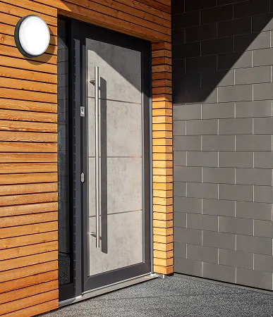 Porte d'entrée moderne en verre avec cadre noir, grande poignée métallique, mur en bois à gauche et mur en briques grises à droite.