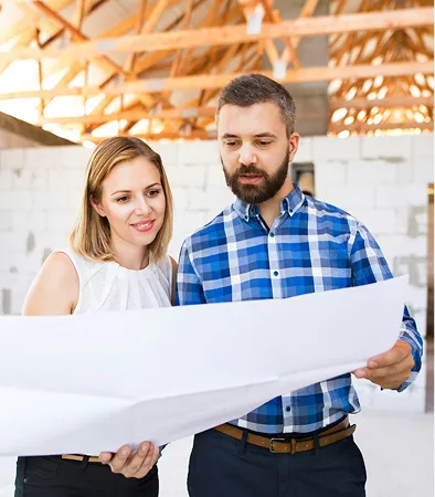 Un homme et une femme examinent un grand plan ou une feuille de papier dans un bâtiment en construction avec une charpente en bois apparente.