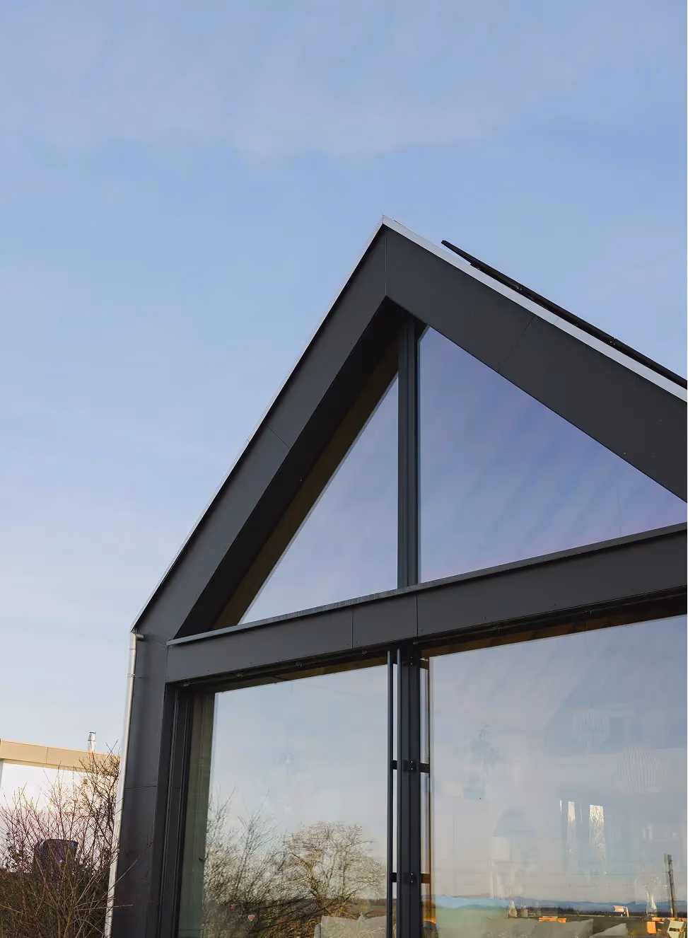 Façade d'une maison moderne Suisse composée de grands panneaux de verre reflétant le ciel, mettant en valeur les fenêtres Domofen SA, un design épuré et une architecture angulaire.