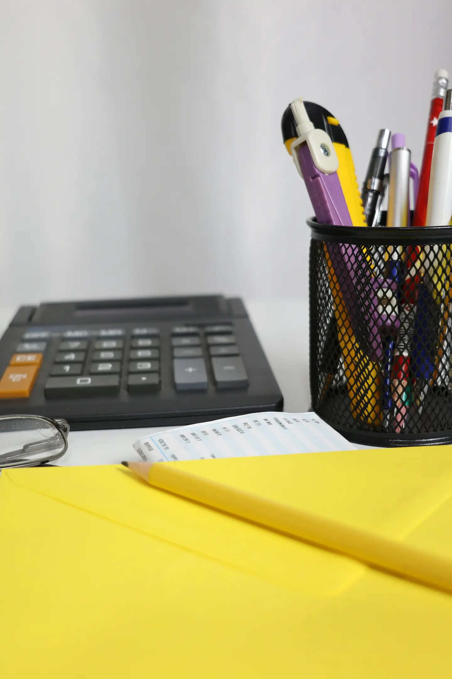 Une calculatrice, un porte-stylo avec des stylos, un crayon jaune et une enveloppe jaune sur un bureau.