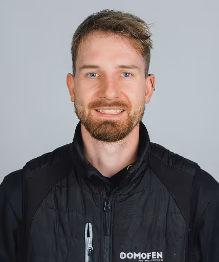 Portrait d'un homme souriant portant une veste noire avec le logo Domofen.