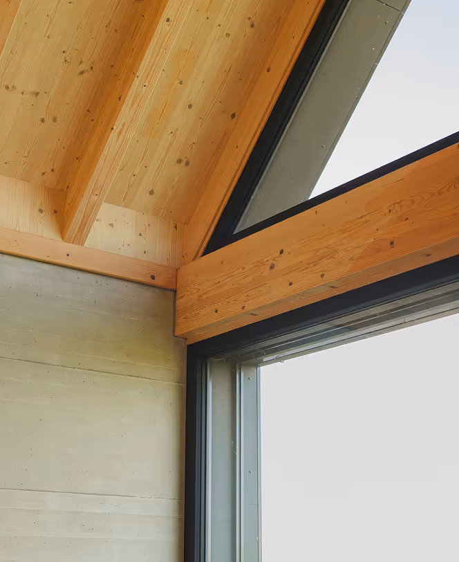 Coin intérieur d'une maison avec plafond en bois clair à poutres apparentes et fenêtre triangulaire moderne.