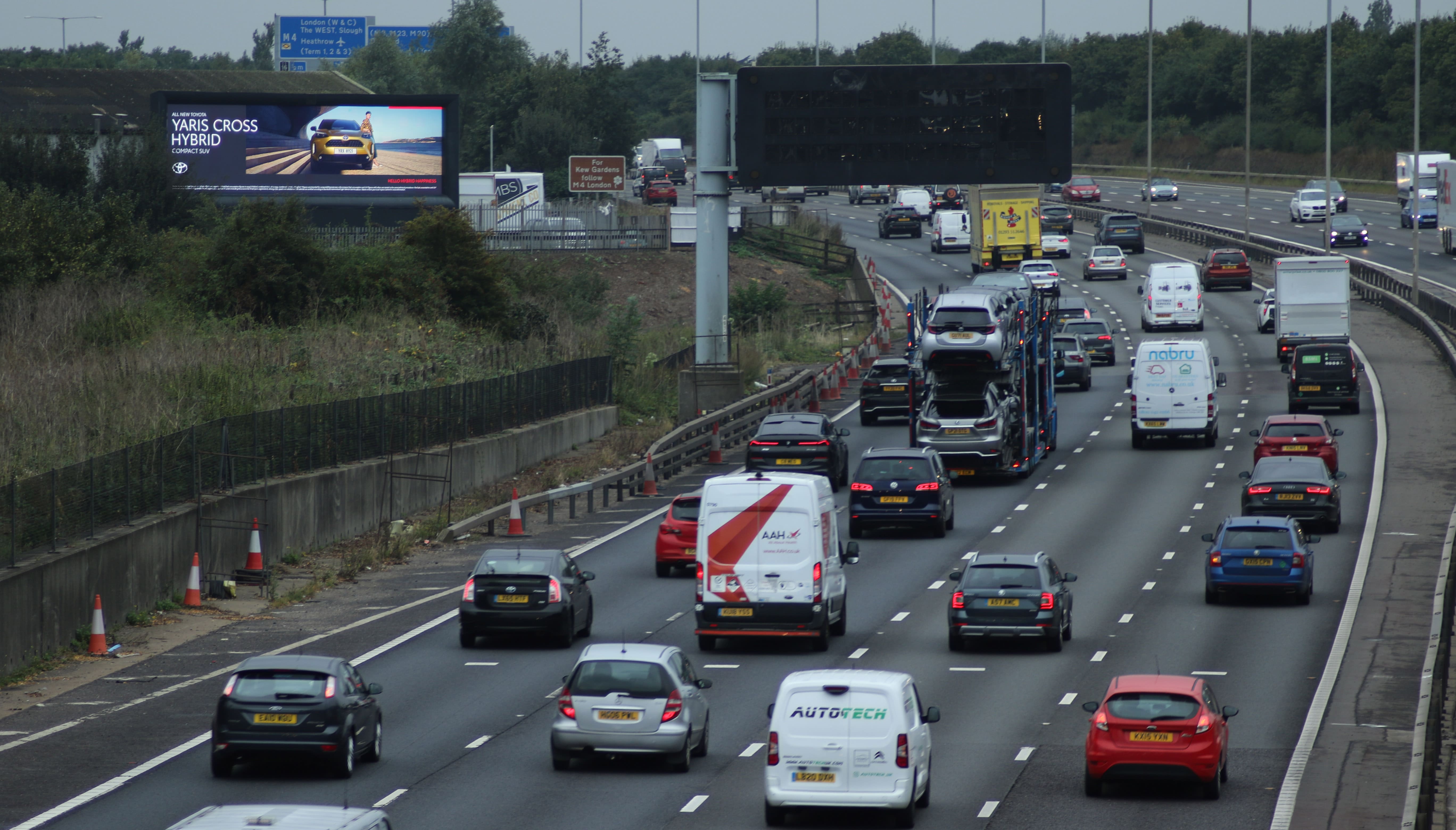 Multi-lane highway with moderate traffic including cars, vans, and a car transport truck under overcast sky.