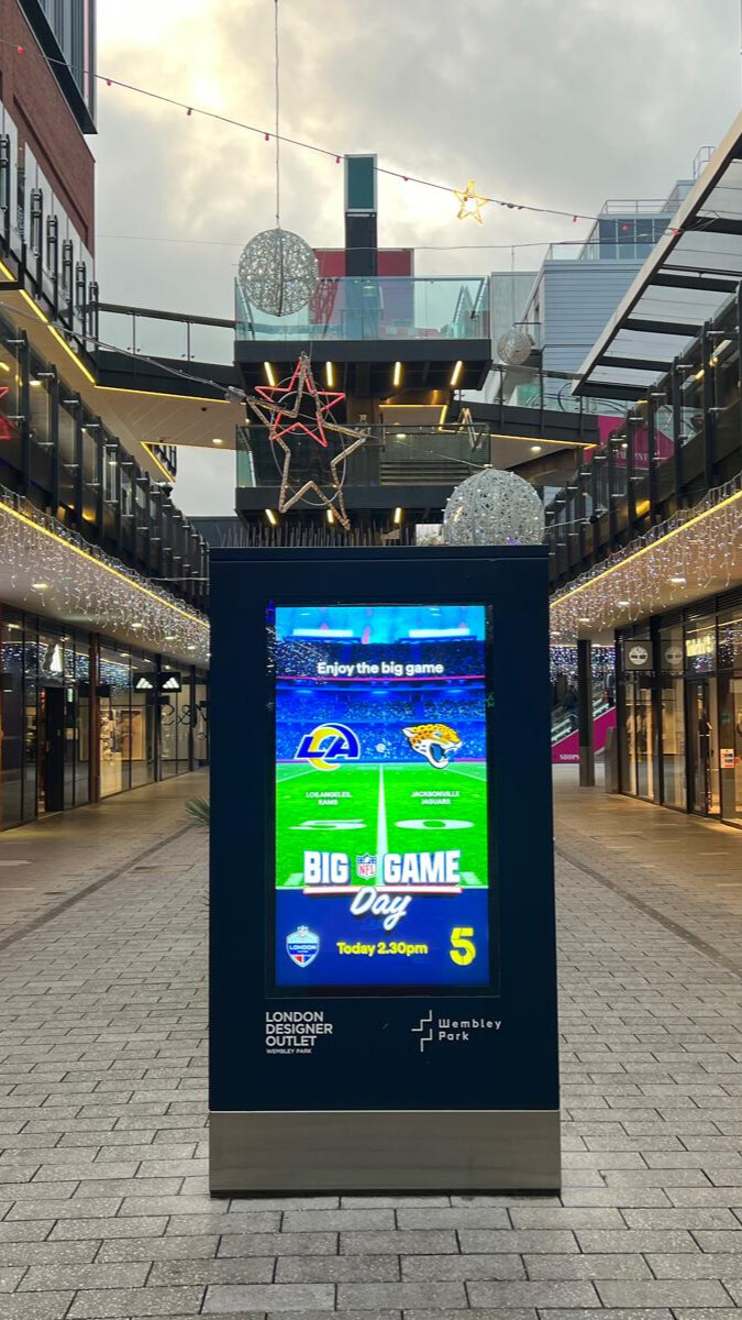 Digital signboard in an outdoor shopping area displaying NFL Big Game Day with Los Angeles Rams vs Jacksonville Jaguars logos and game time.