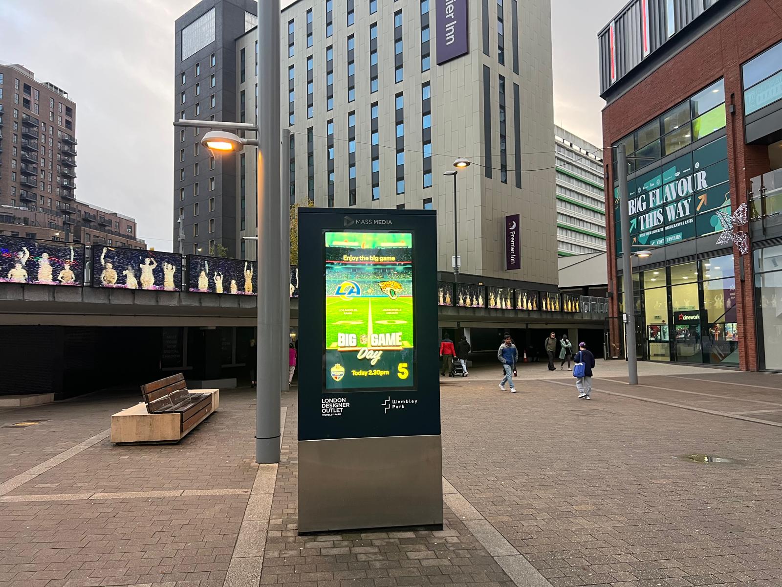Digital billboard in an urban plaza advertising NFL Big Game Day between Los Angeles Rams and Jacksonville Jaguars, with surrounding buildings and pedestrians.