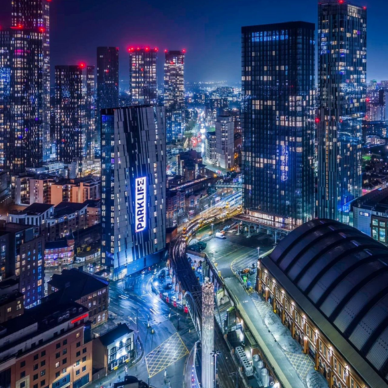 Night cityscape with illuminated high-rise buildings and a tall building displaying a vertical PARKLIFE sign.