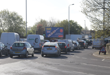 Traffic congestion with multiple cars and vans waiting near a roundabout on a sunny day.