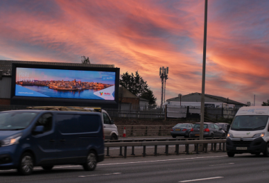 Busy highway with vehicles passing by a large digital billboard under a colorful sunset sky.