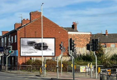 Urban street intersection with traffic lights, brick buildings, and a billboard featuring black and white images of cars.