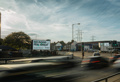 Busy road with blurred moving cars under a partly cloudy sky and a billboard that reads 'Do Good Feel Great'.