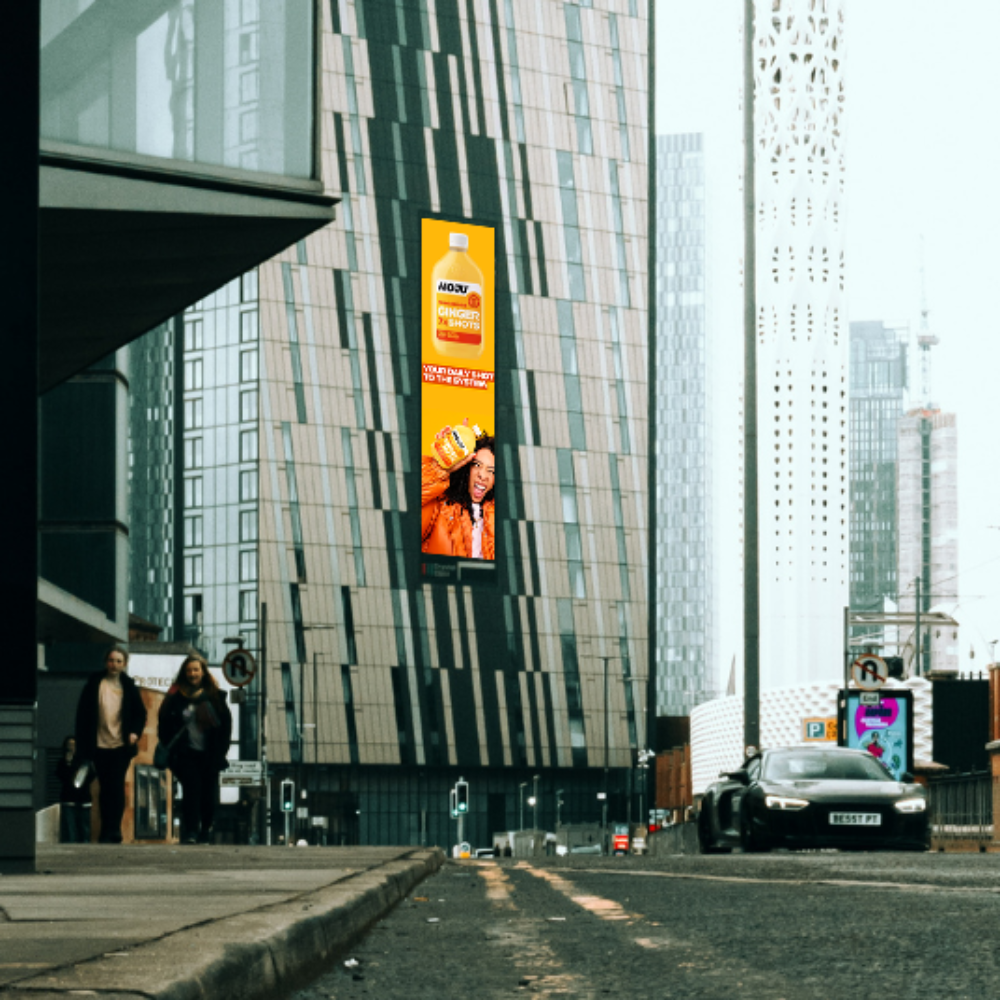Tall building with vertical digital billboard showing Moju Ginger 28 Shots juice and a smiling woman.