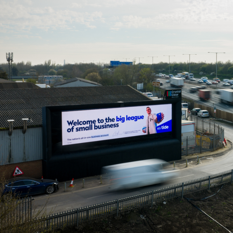 Traffic on a suburban street with a digital billboard featuring an Oasis live '25 concert advertisement.