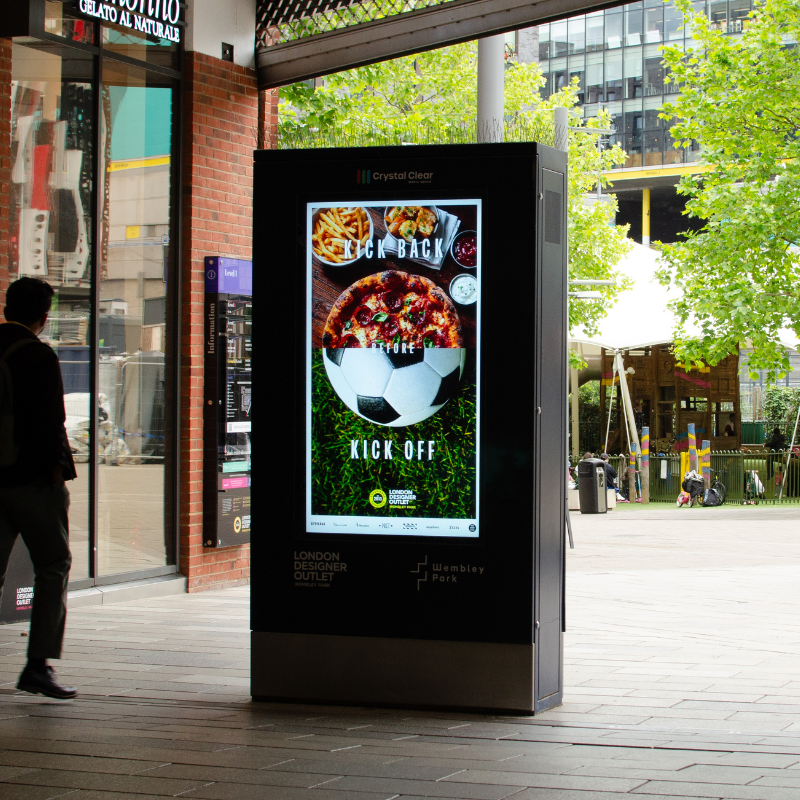 Digital advertising board in a shopping area displaying a smiling soccer player in a yellow Real Madrid jersey with logos for Prime and UEFA Champions League above.