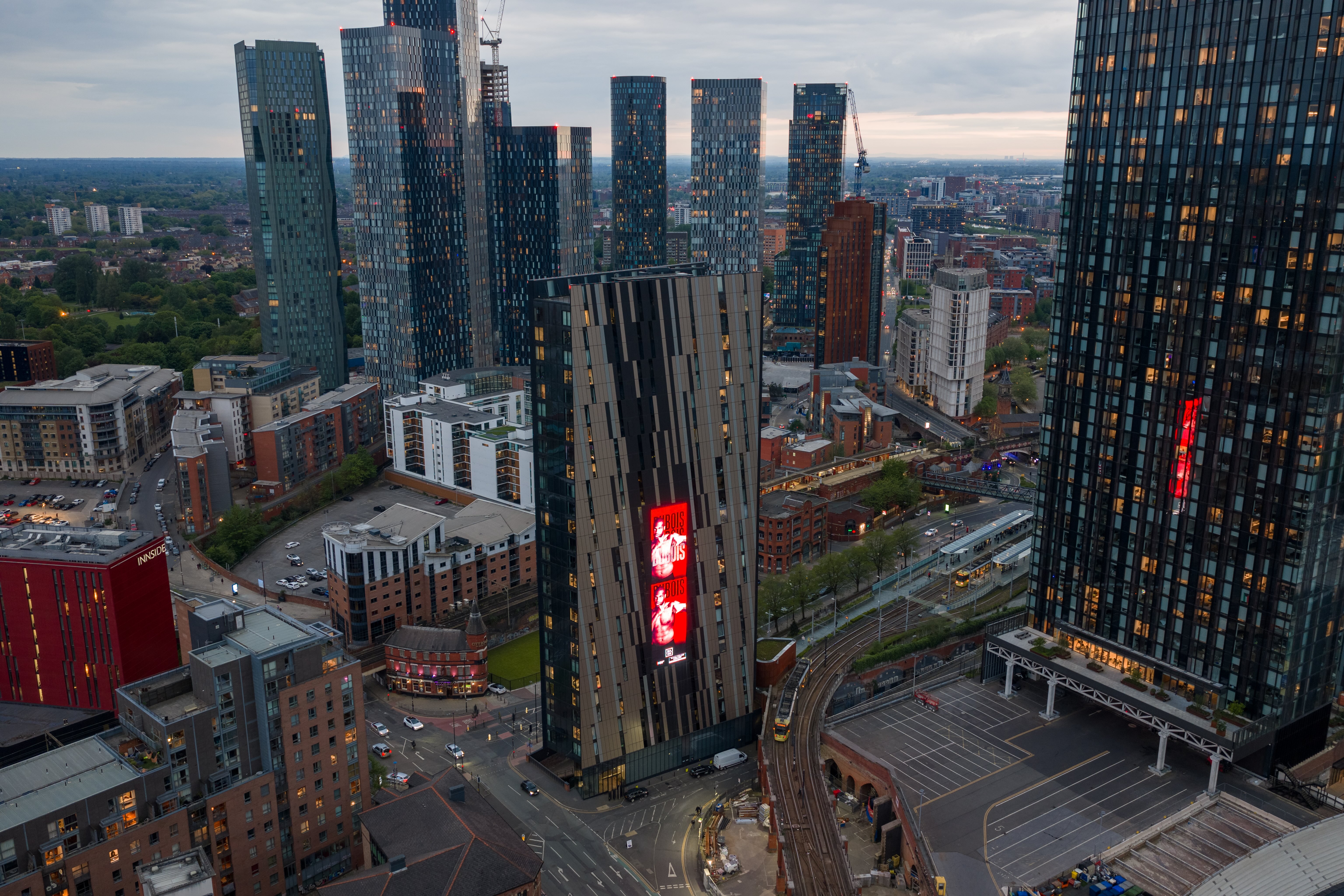 City skyline at dusk with modern skyscrapers and a tall building displaying a red digital advertisement.