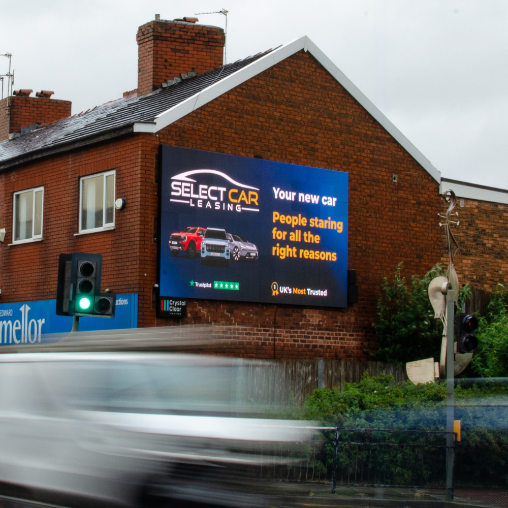 Digital billboard on brick building advertising Select Car Leasing with images of three cars and slogan.