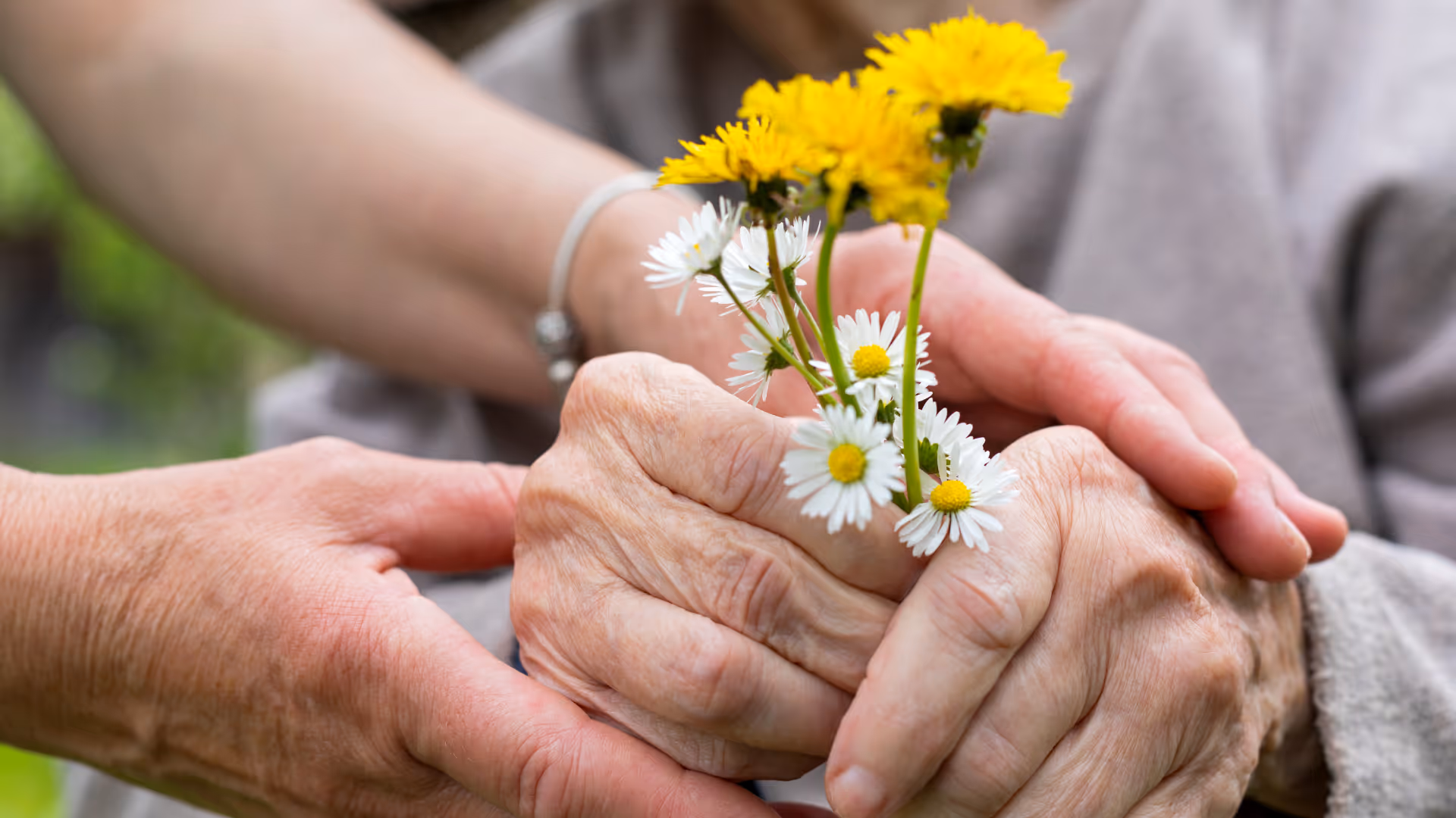 An elderly man with a cane walks arm-in-arm with a woman carrying a reusable grocery bag on a park path.