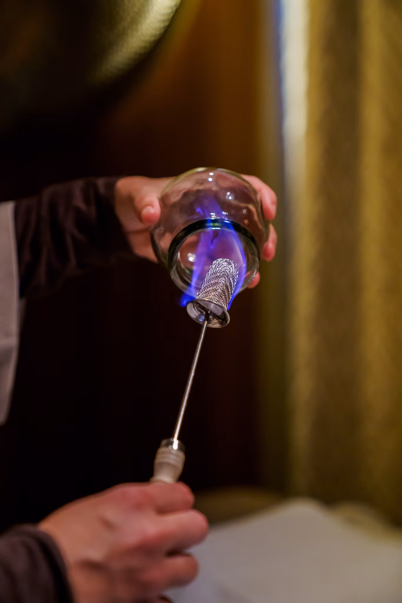 Iemand gebruikt een brander met blauwe vlam om een glazen cup te verwarmen. Firecupping.