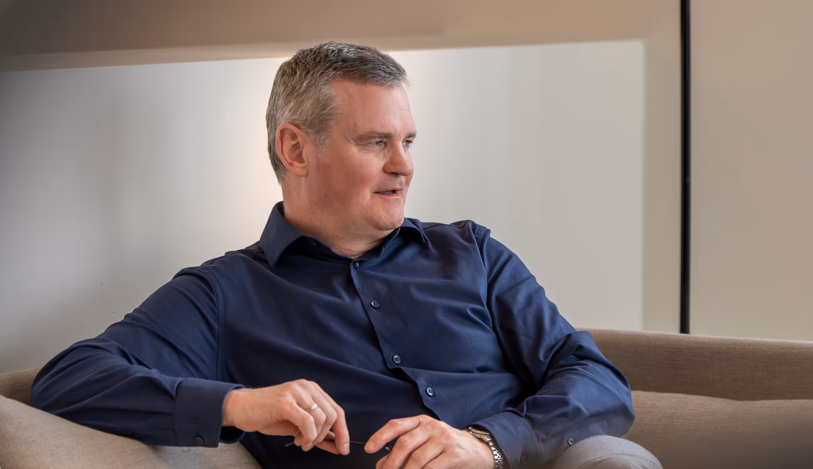 Man in donkerblauw hemd die rustig in gesprek is in een moderne kantoorruimte.