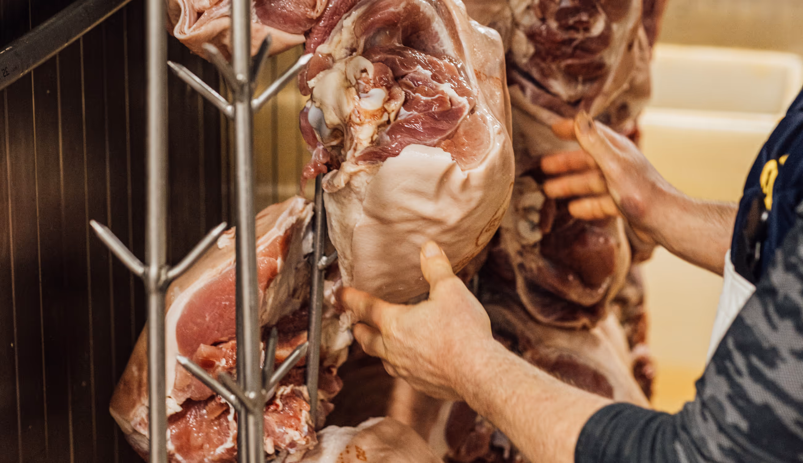 Close-up van handen die een groot stuk rauw vlees ophangen in de productieruimte.