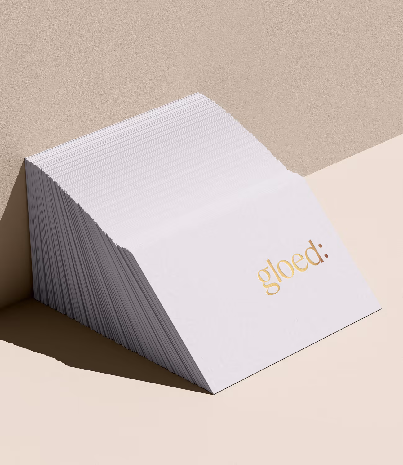 Verschillende witte visitekaartjes met het logo ‘gloed:’ in goudkleurige folie op een zachte zandkleurige achtergrond. De compositie oogt rustig en verfijnd.