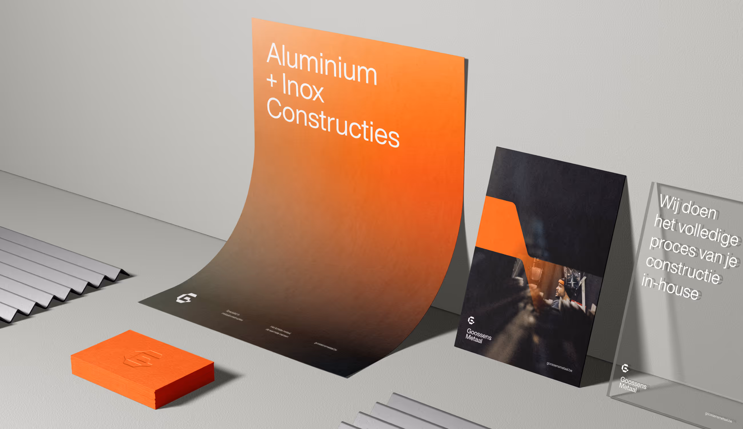 Verschillende drukwerken van Goossens Metaal: een oranje visitekaartje, posters en brochures met sterke typografie en industriële esthetiek. Het beeld straalt kwaliteit en precisie uit.