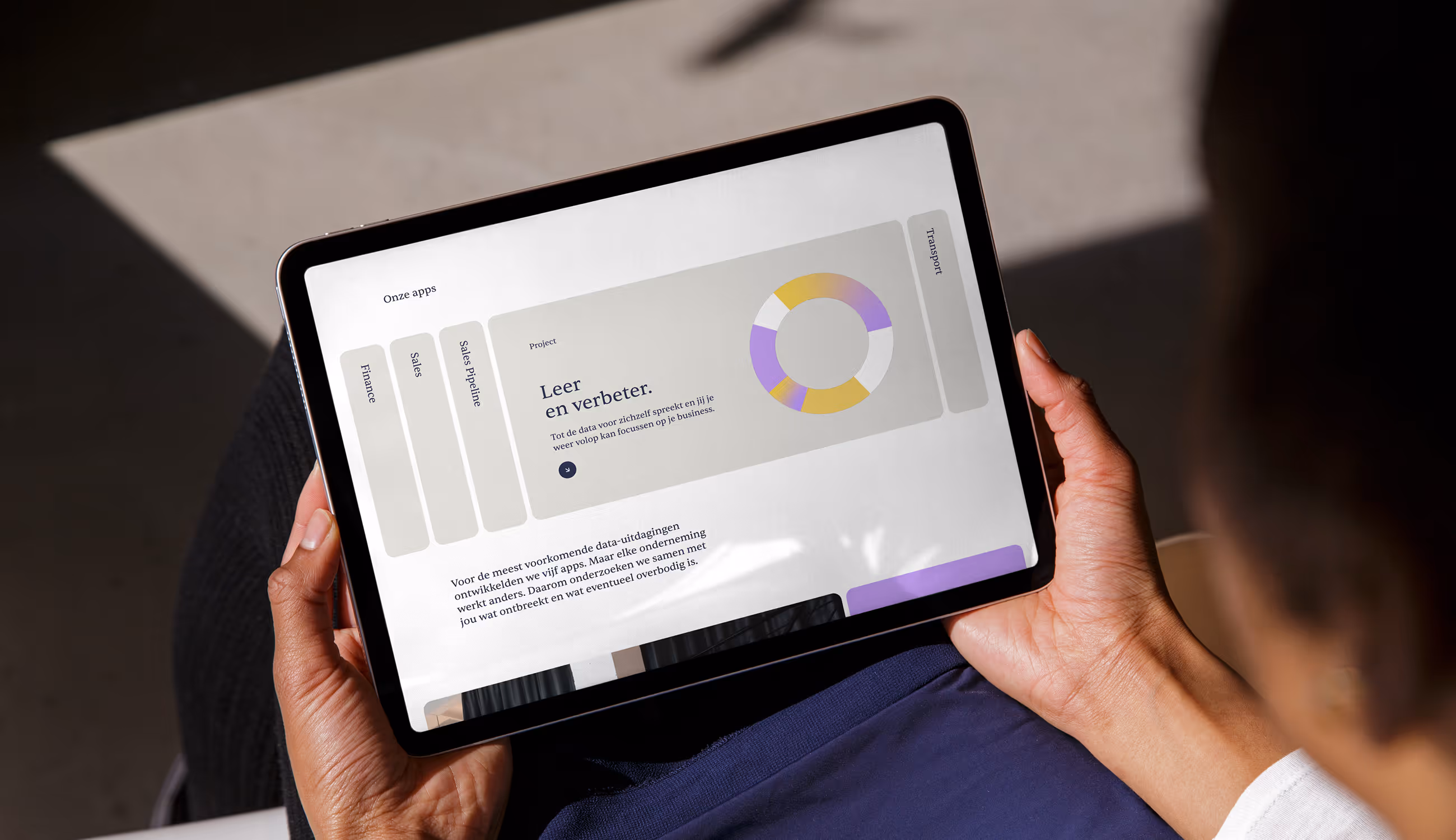 Een persoon houdt een tablet vast met een app van InsightData. Op het scherm staat een donutgrafiek in paars-geel en de tekst “Leer en verbeter.”