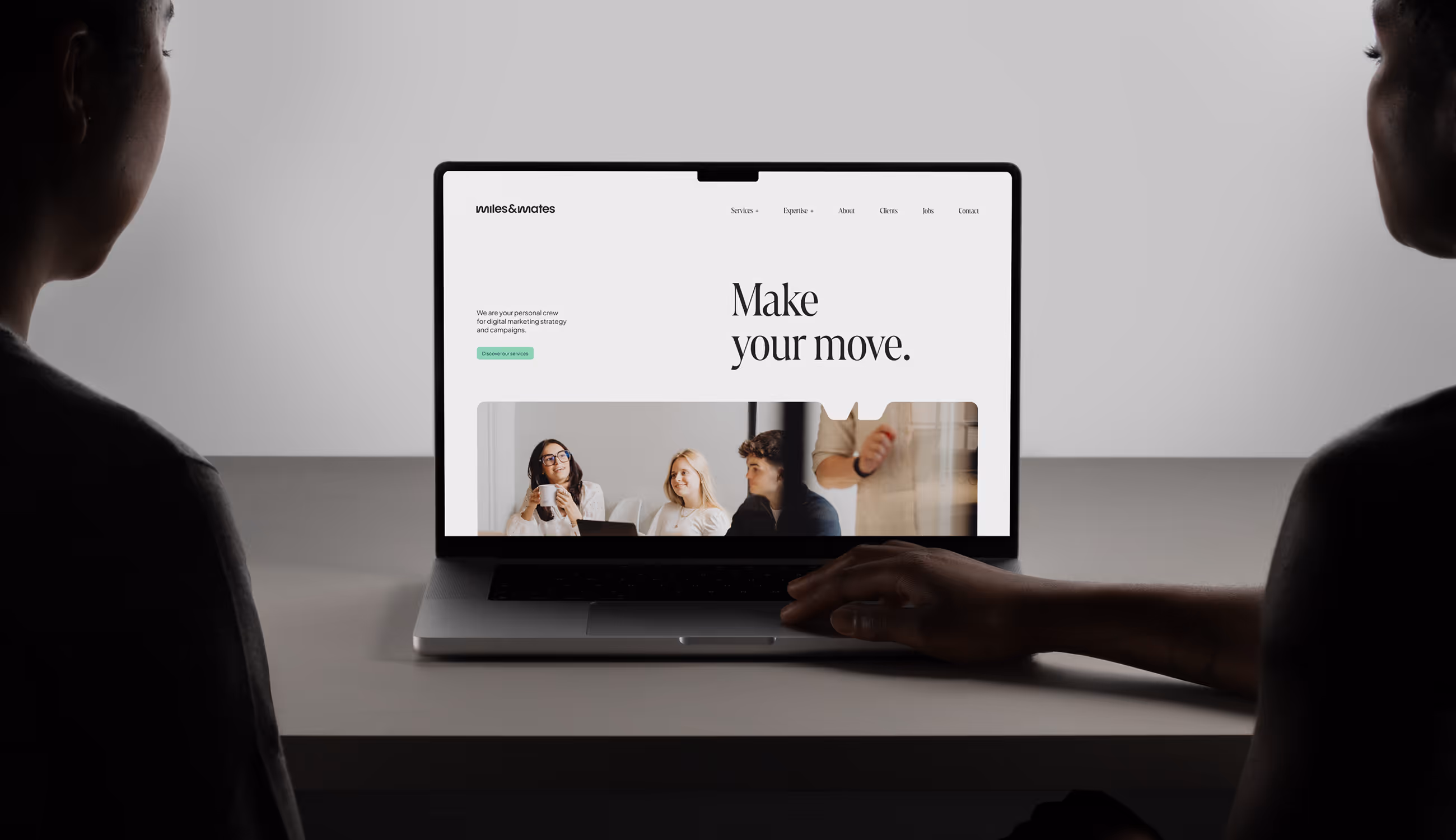 Twee personen kijken naar de Miles & Mates-website op een laptop met de slogan “Make your move.” en foto van een teamvergadering.