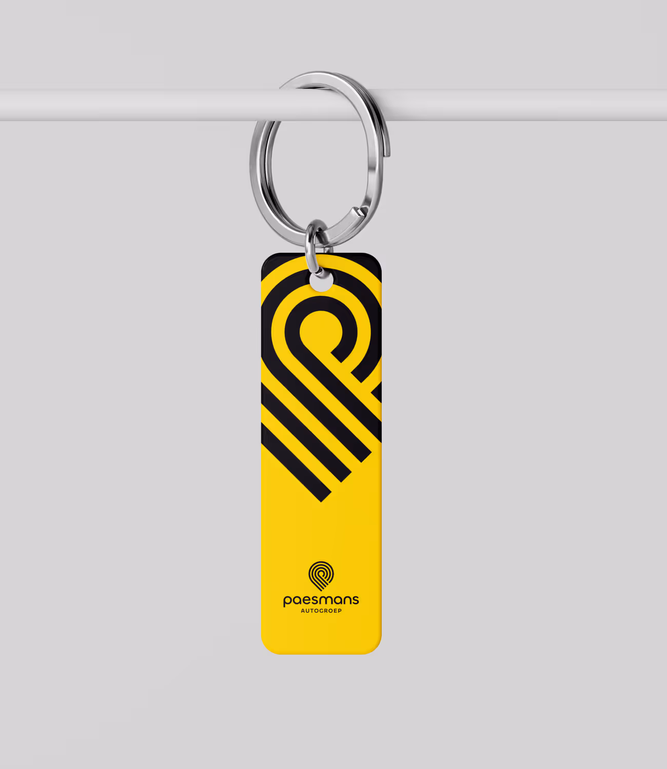 Gele sleutelhanger met zwart grafisch patroon en Paesmans-logo, bevestigd aan een metalen sleutelring.