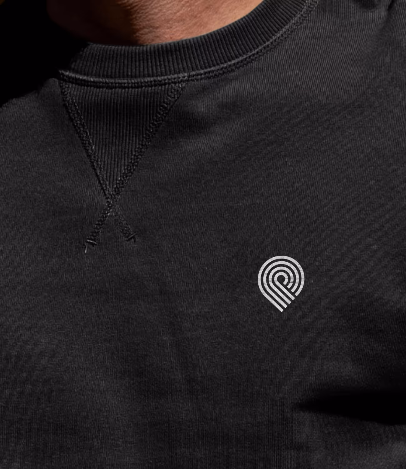 Close-up van een zwarte trui met het witte Paesmans-logo subtiel geborduurd op de borst.