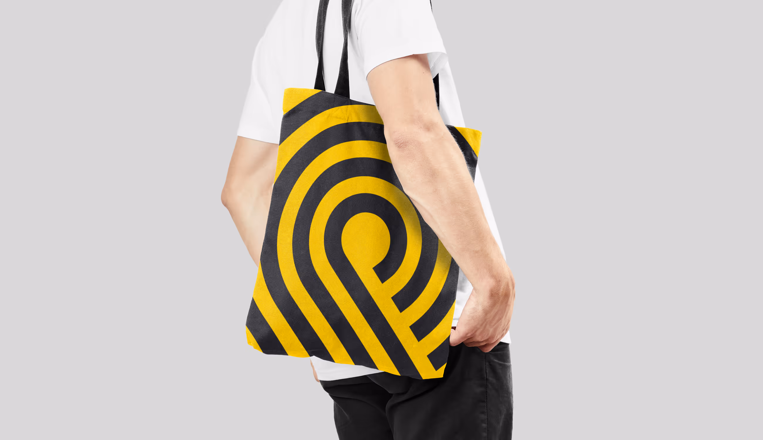 Een persoon draagt een gele linnen tas met het grafische zwarte Paesmans-patroon op een lichtgrijze achtergrond.