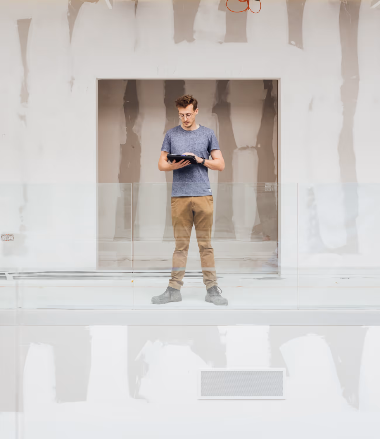 Man op werf bekijkt plannen op een tablet, omringd door onafgewerkte muren en lichtinval van boven.