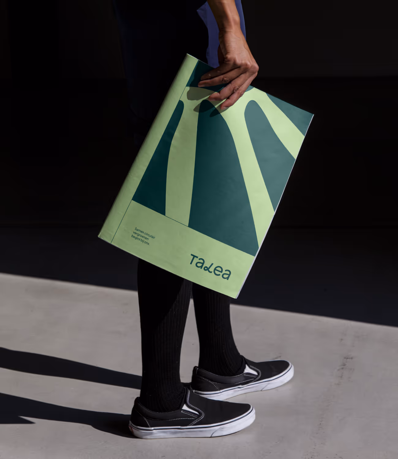 Iemand houdt een groot gedrukt rapport met Talea-branding vast, in natuurlijke kleuren en zachte belichting.