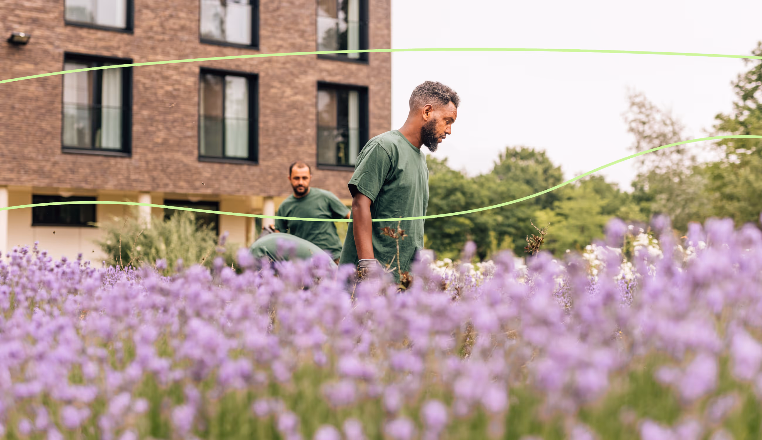 Twee medewerkers aan het werk in een bloemenveld bij een modern gebouw, omgeven door lavendel en groen.