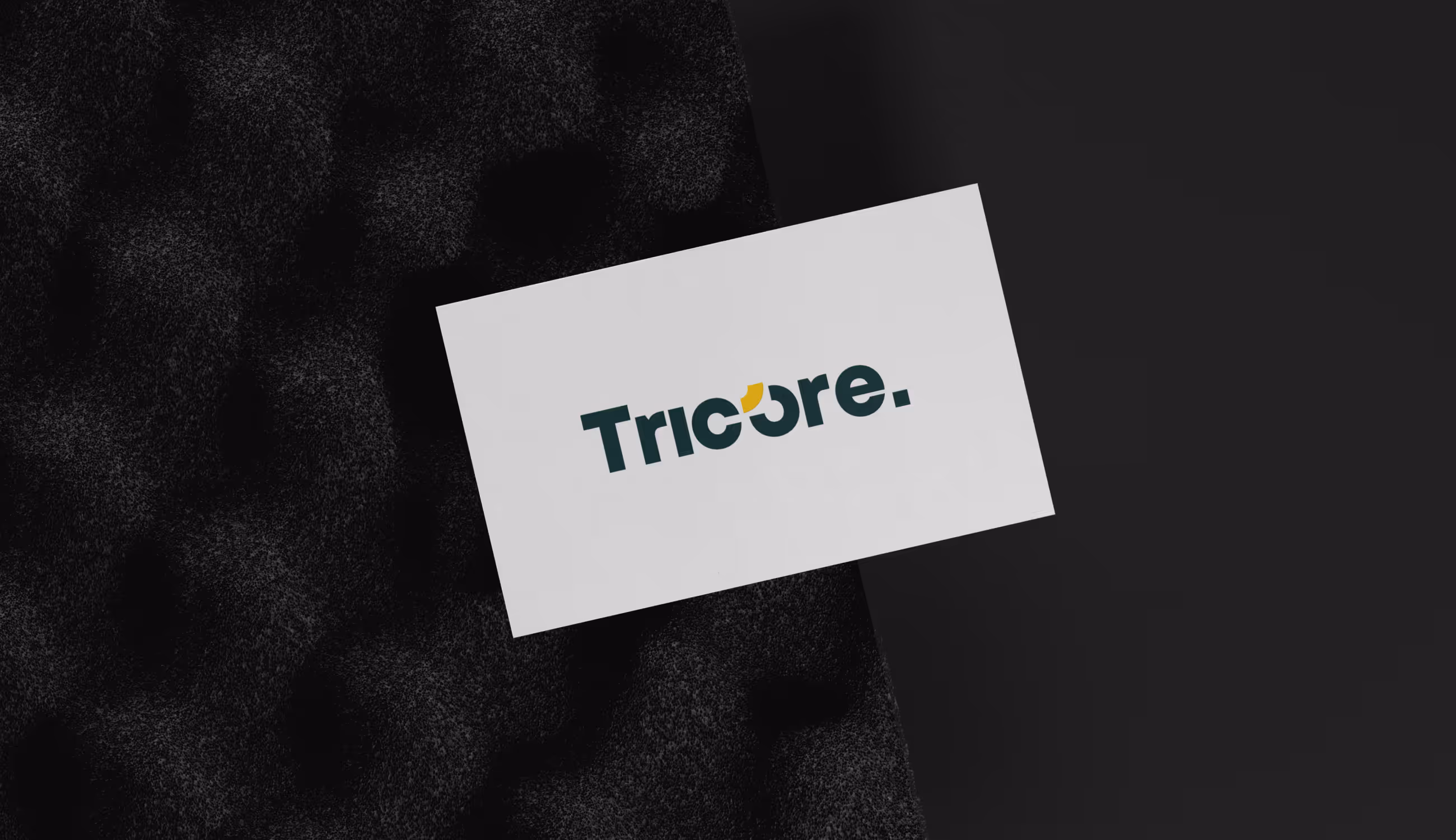 Witte visitekaart met Tricore-logo op donkere textuur, minimalistisch gepresenteerd.