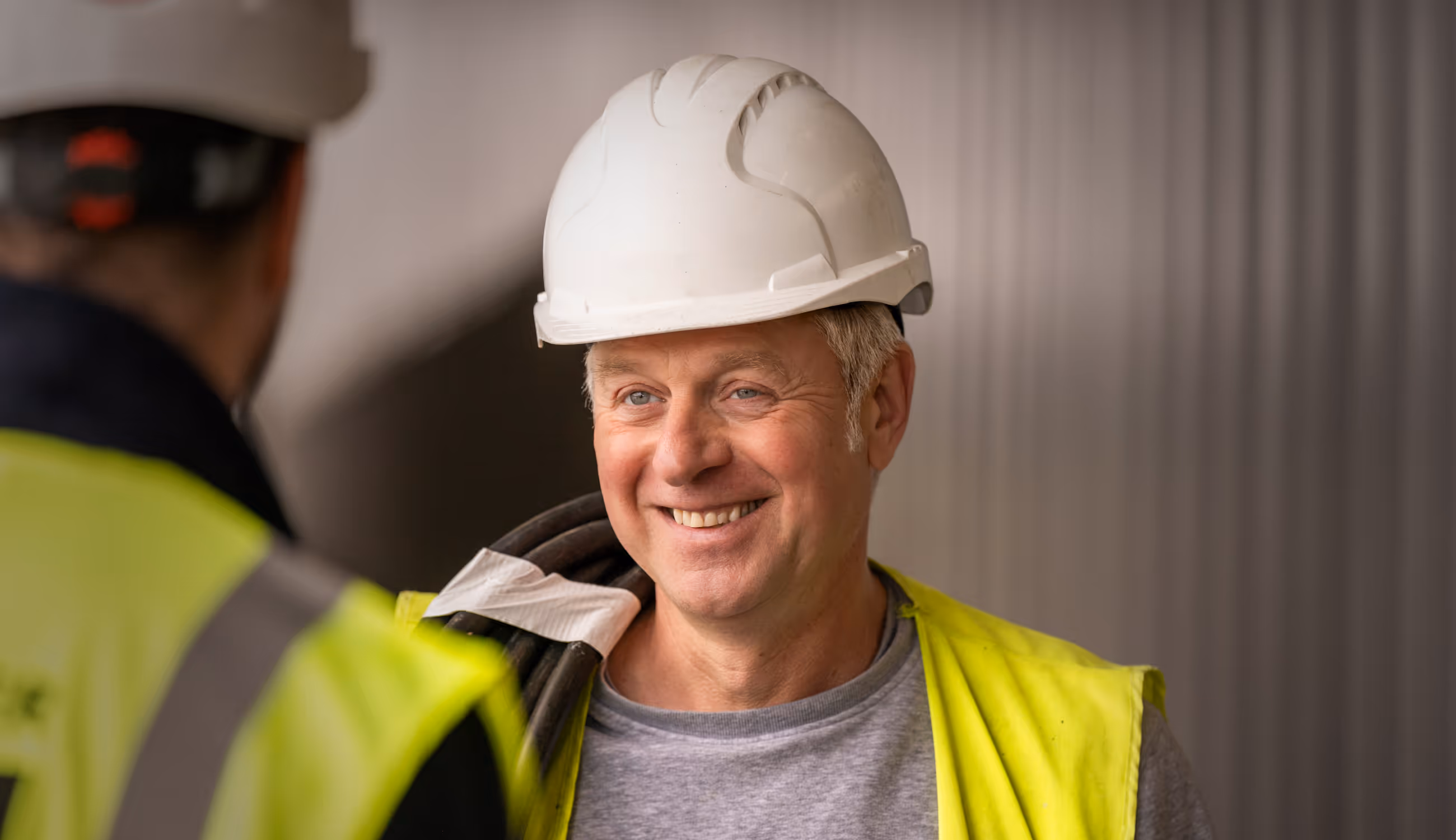 Portret van Warsco-medewerker met witte helm en fluohesje, glimlachend terwijl hij met collega praat.