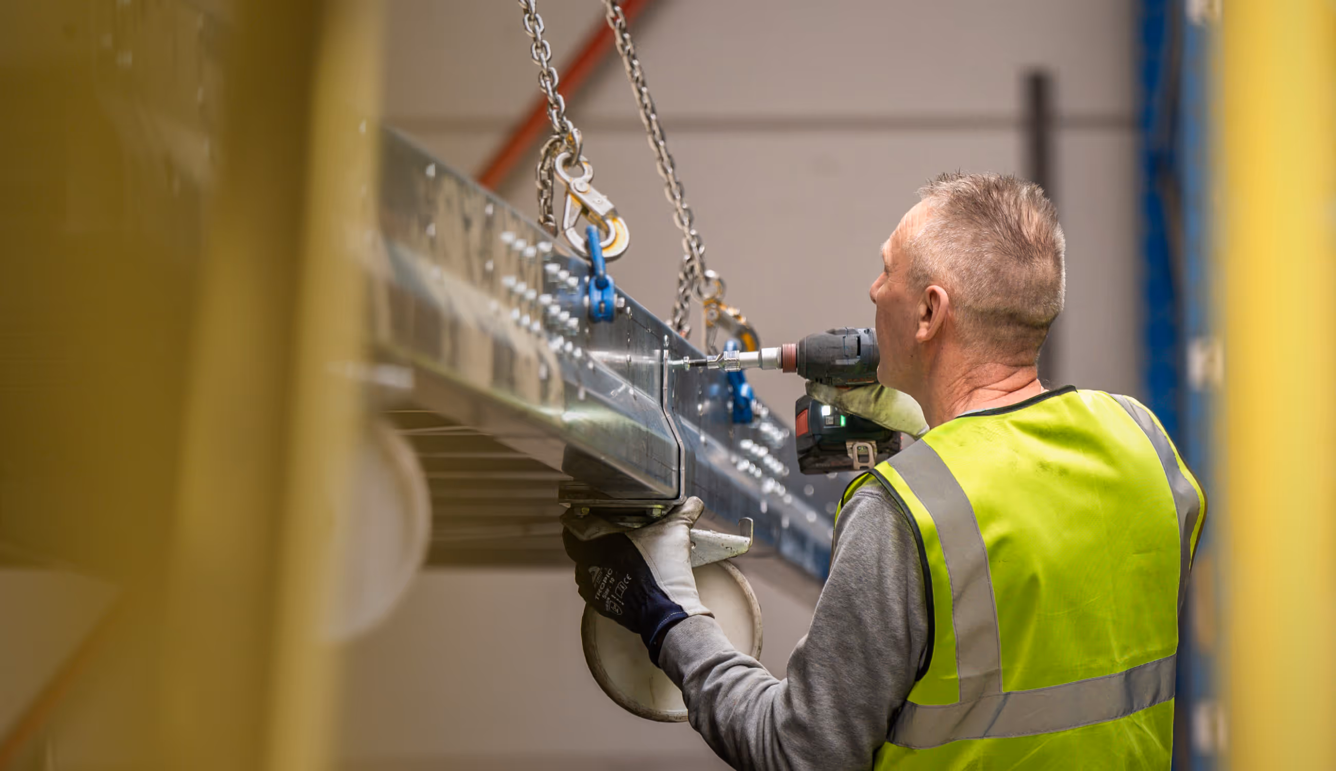 Warsco-medewerker bevestigt metalen structuur met boormachine, geconcentreerd aan het werk in de fabriek.