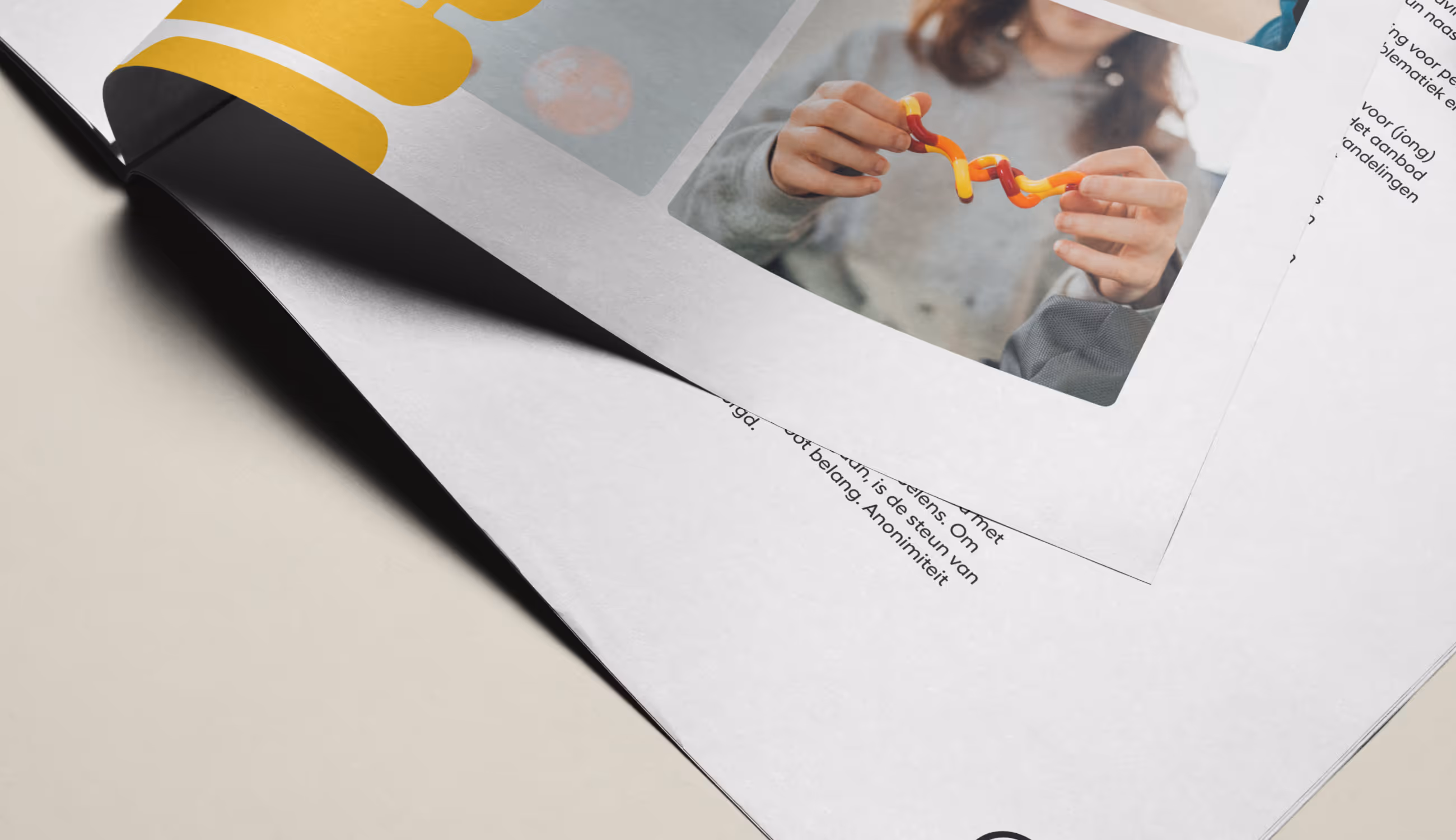 Detailfoto van opengevouwen brochure waarin een persoon een oranje-geel voorwerp vasthoudt, symbool voor interactie en herstel.