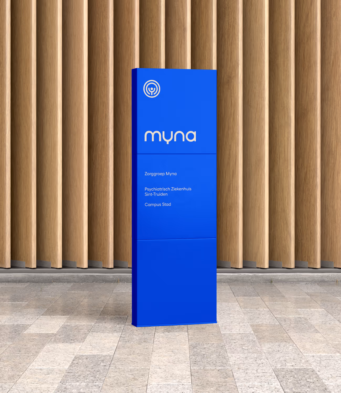 Blauwe informatiezuil met Myna-logo en tekst “Zorggroep Myna – Psychiatrisch Ziekenhuis Sint-Truiden – Campus Stad” tegen houten wand, straalt vertrouwen en helderheid uit.