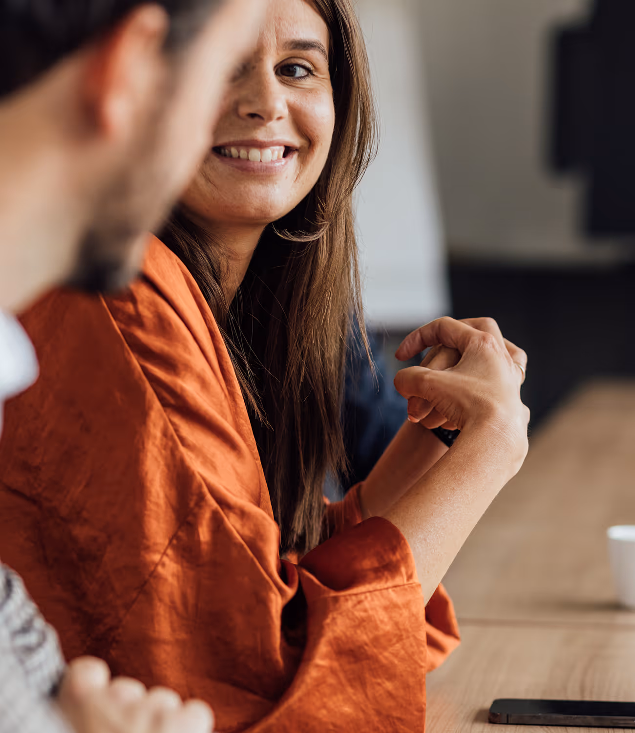 Vrouw glimlacht tijdens overlegmoment aan tafel.
