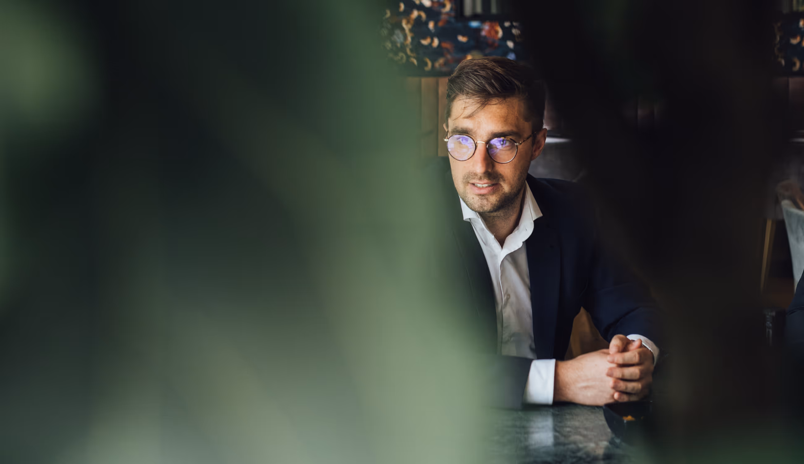 Man in pak achter planten gefotografeerd tijdens gesprek.