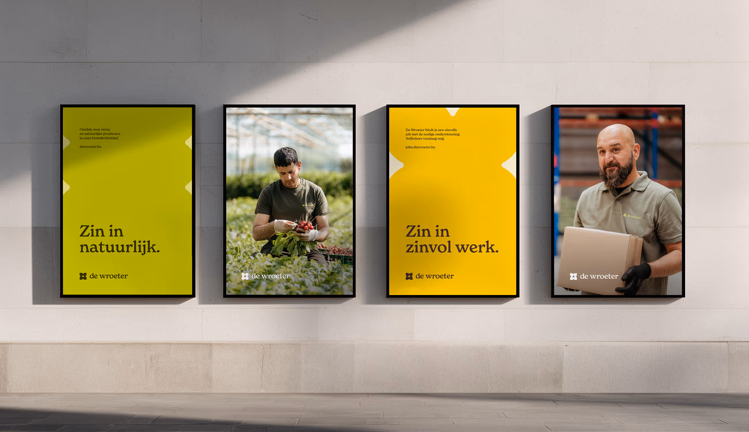 Vier De Wroeter affiches naast elkaar met campagnezinnen en portretten van medewerkers in een moderne publieke ruimte.