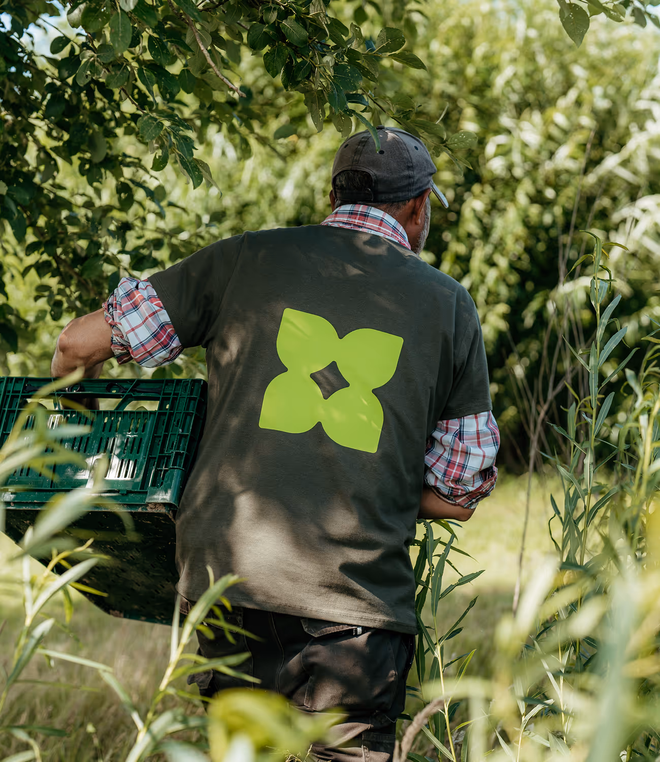 Medewerker van De Wroeter draagt werkkledij met groot groen logo op de rug tijdens buitenwerk.
