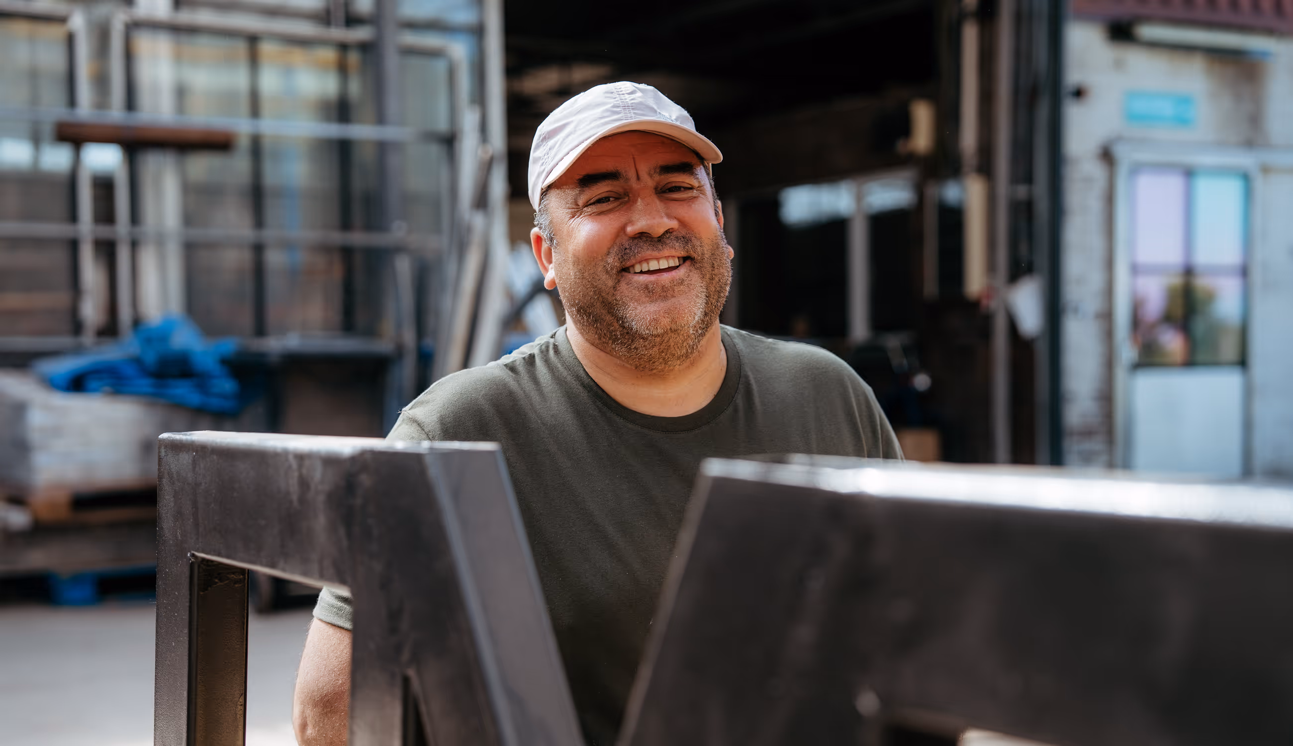 Portret van een lachende medewerker van De Wroeter op de werkvloer tussen materialen.