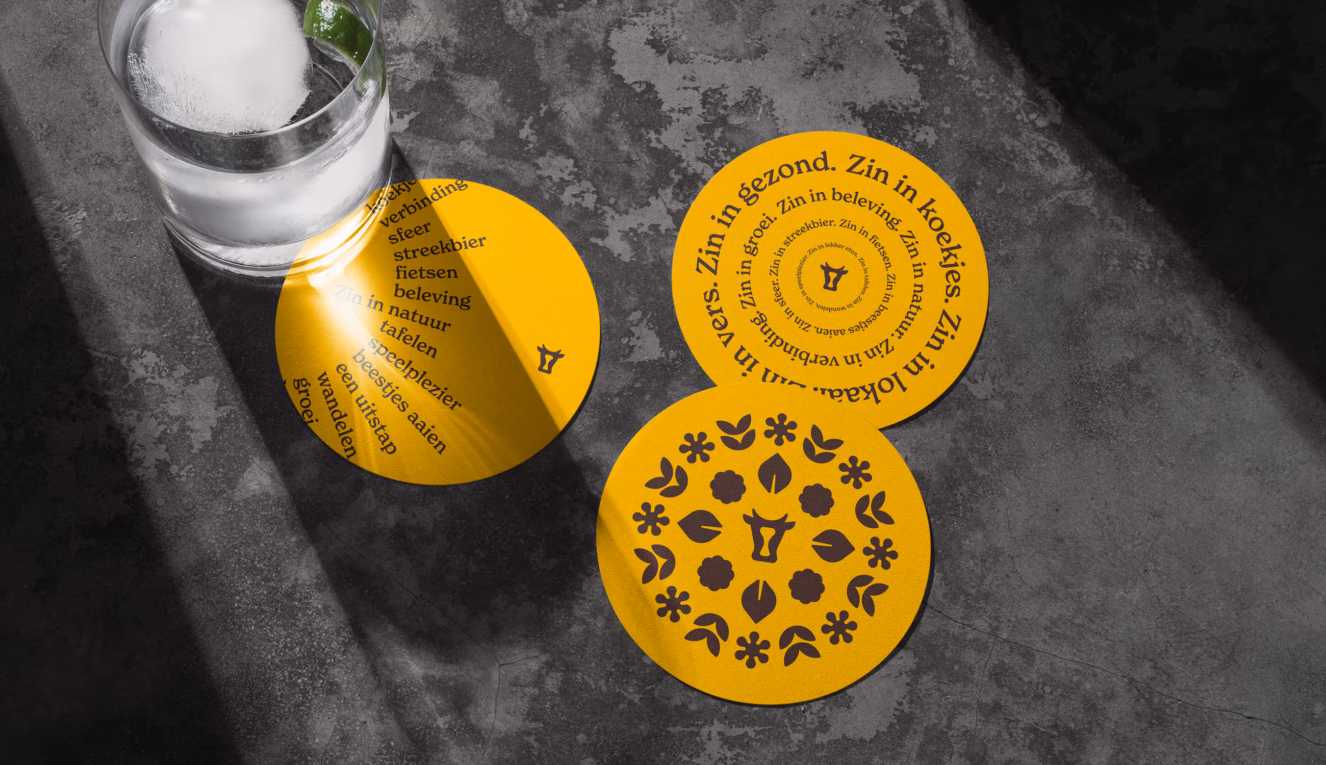 Gele Koe-Vert bierviltjes met woorden rond zin, natuur en beleving op een donkere tafel.