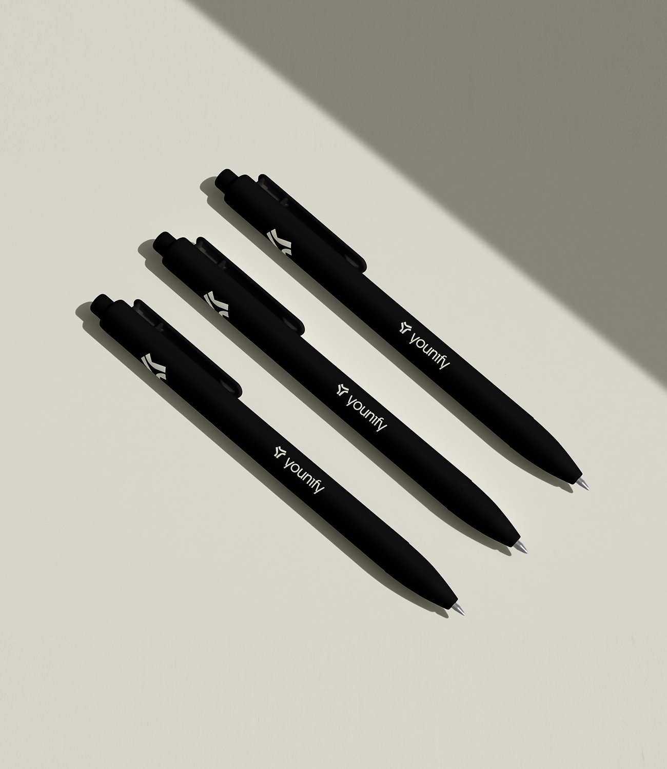 Drie zwarte Younify-pennen met wit logo op een lichte minimalistische ondergrond met sterke schaduwen.