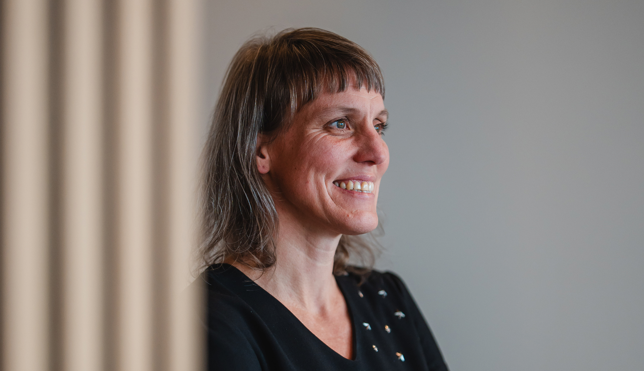 Portret van een glimlachende vrouwelijke consultant in een zachte en minimalistische kantooromgeving met neutrale tinten.