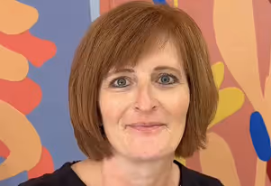 Smiling woman with short red hair in front of a colorful abstract background.