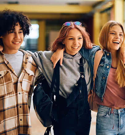 Three teenagers walking together indoors with arms around each other, smiling and happy.